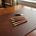 5 Rosewood Gel Rollerball pens with gold tips on a Regency-style writing desk