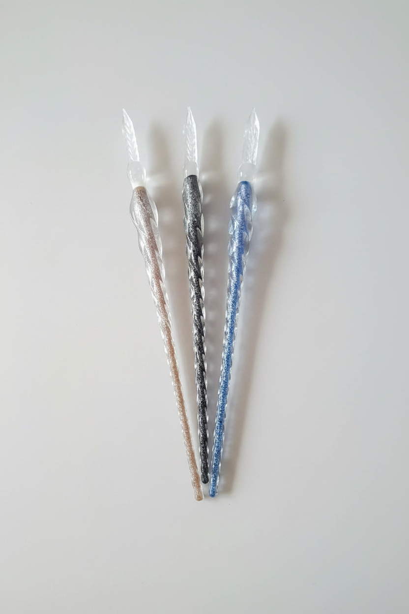 Three glitter glass fountain pens on a plain light background